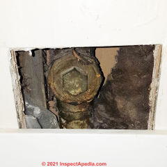 Fiberglass and other materials at a bathroom plumbing drain access (C) InspectApedia.com BPA