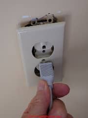 Loose electrical receptacle cover can fall on to wall plug contacts (C) Danie Friedman at InspectApedia.com