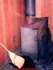 Photograph of a woodstove too close to paneling, a fire hazard at both the woodstove and its metal flue.