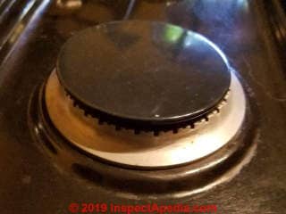 Gas burner cap is crooked on the burner base, causing failure of the gas igniter or a lopsided and dangerous flame (C) Daniel Friedman at InspectApedia.com