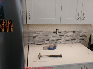 Tile backsplash begins at one end, pressed into mastic and using tile spacers as needed (C) InspectApedia.com A Church