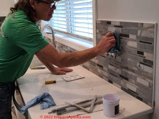 Wiping off excess grout, installing a ceramic tile kitchen backsplash (C) InspectApedia.com A Church