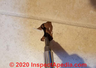 Removing debris from the hole accidentally punched into a ceramic floor tile (C) Daniel Friedman at InspectApedia.com