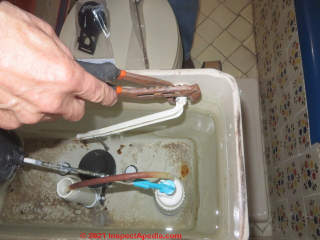 Unscrewing the lock nut that holds a toilet flush lever in place (C) Daniel Friedman at InspectApedia.com