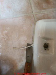 A putty knife safely removes caulk sealant from around the toilet base when taking out an old toilet (C) Daniel Friedman at InspectApedia.com