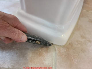 Use a utility knife to cut caulk or sealant at the toilet base IF the floor is tile - don't do this on vinyl or wood. (C) Daniel Friedman at InspectApedia.com