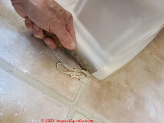 A putty knife safely removes caulk sealant from around the toilet base when taking out an old toilet  (C) Daniel Friedman at InspectApedia.com