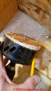 Removing the wooden plug from a round hole saw during Cinderella toilet installation  - (C) Daniel Friedman at InspectApedia.com