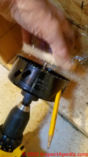 Removing the wooden plug from a round hole saw during Cinderella toilet installation  - (C) Daniel Friedman at InspectApedia.com