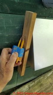 Using the pencil scribe tool to mark the curved cut lines to saw a filler block to mount a flat cover to a curved log wall  - (C) Daniel Friedman at InspectApedia.com