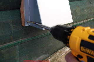 Carefully screw the cover plate flanges through the filler block and into the log wall.  - (C) Daniel Friedman at InspectApedia.com